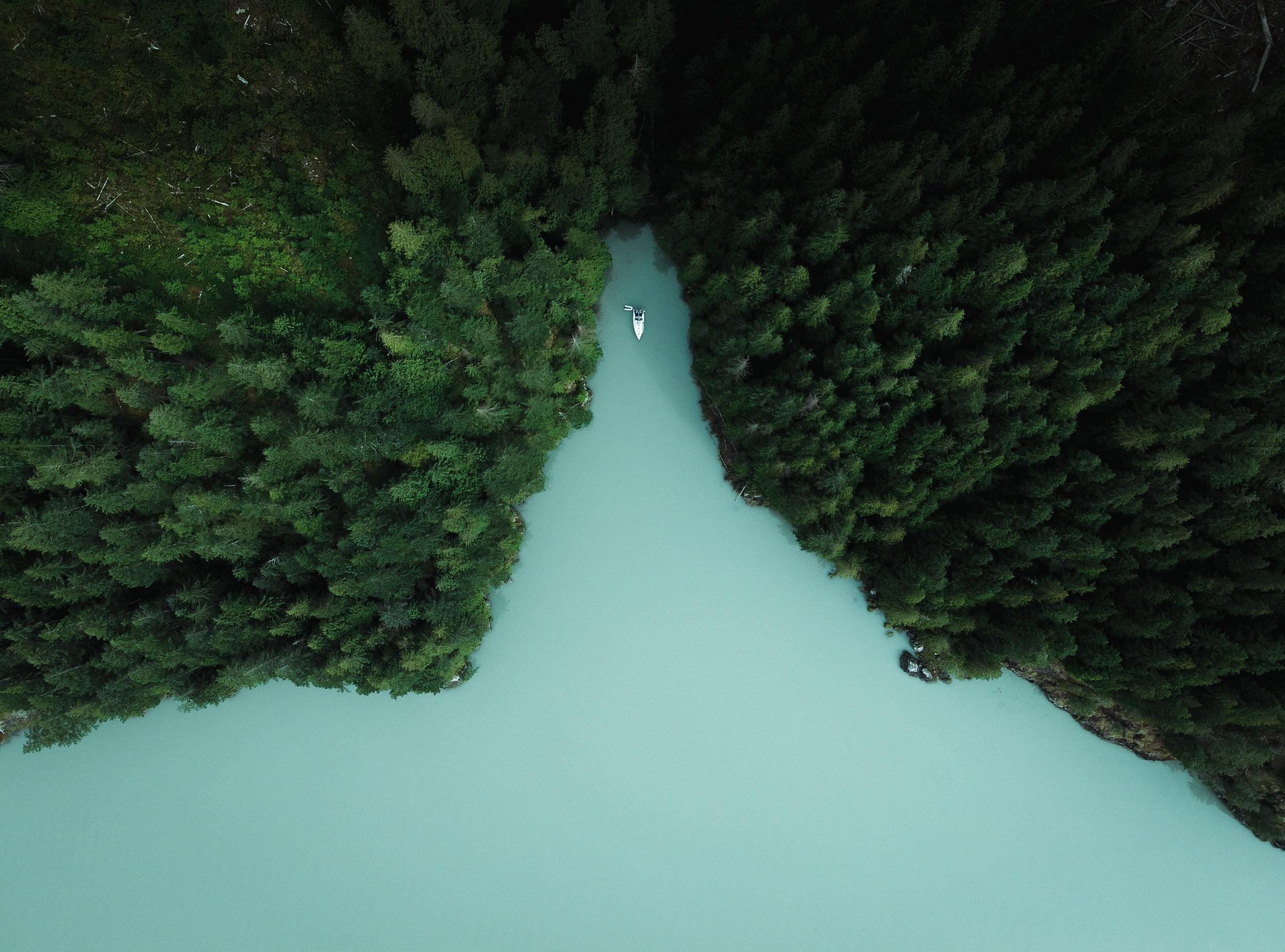 A small sailboat anchored in a narrow green inlet on the BC coast.